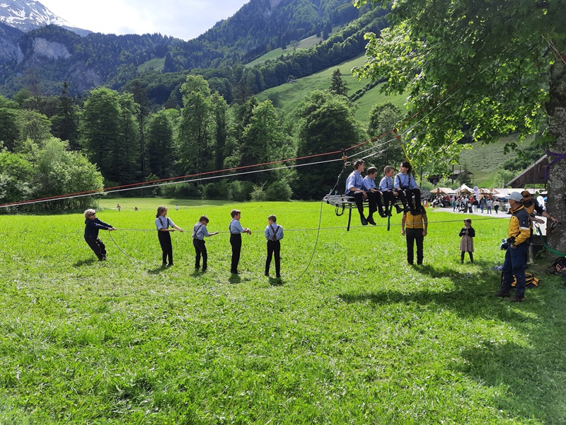 Einige Kinder sitzen auf Seiltragekorb, die anderen halten das Seil